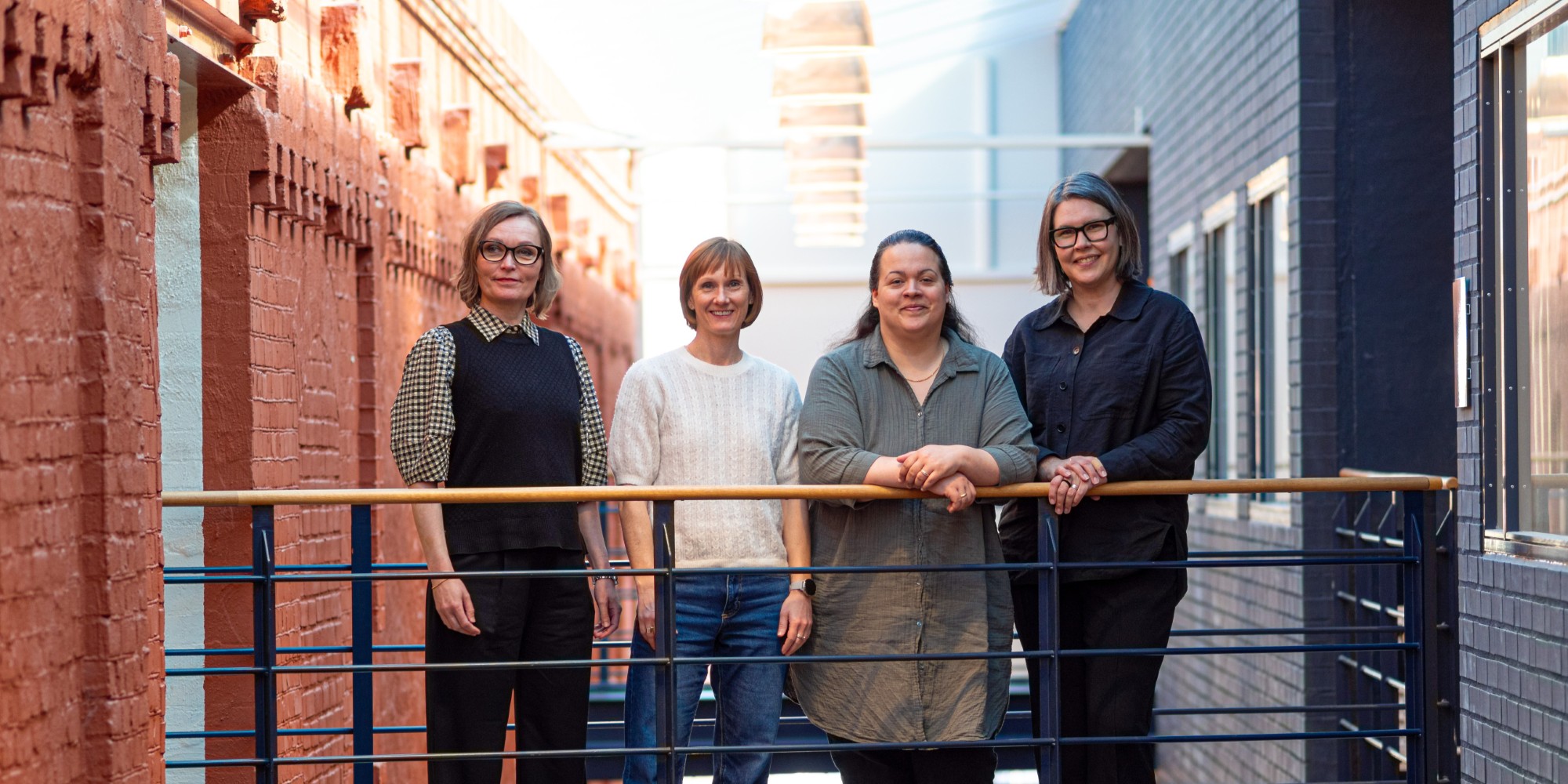 Four people standing against a railing under a glass roof with the sunlight from above