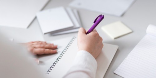 A person writing with a purple pen in a notebook