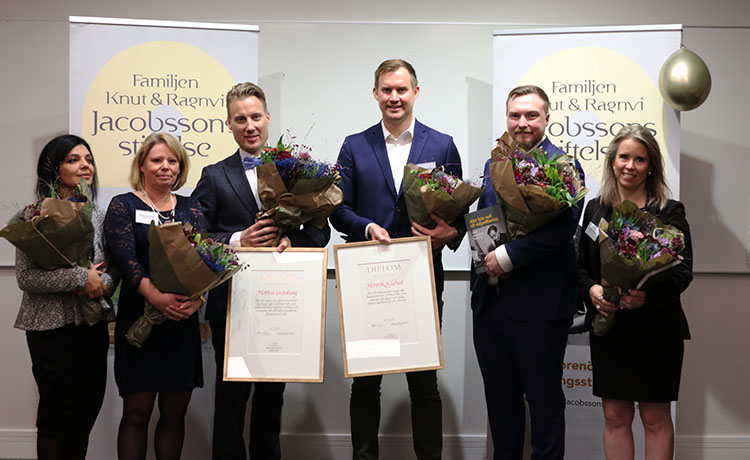 Gruppbild med pristagare som håller i blombuketter framför två roll-ups med texten: Familjen Jacobssons Stiftelse