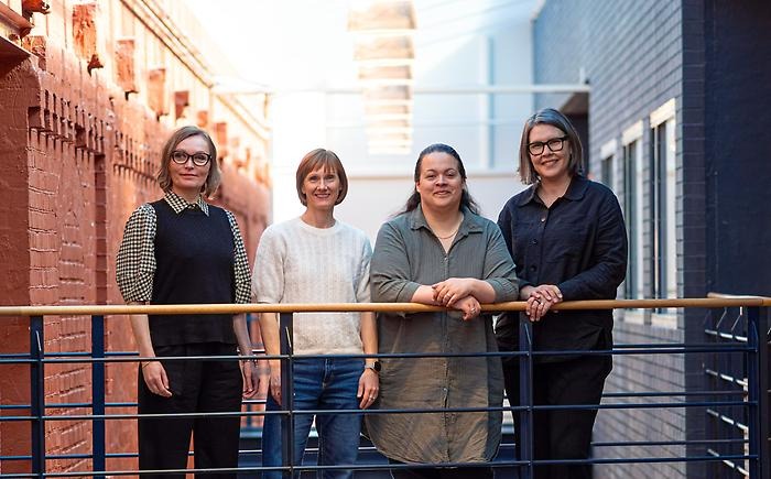 Four women standing in a building. Light is coming through the ceiling above.