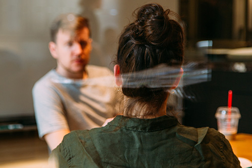 View of the back of a woman sitting at a table opposite a man. 