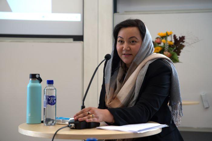 Photo of Rida Ijaz speaking at her PhD defence, standing at a podium with notes and water bottles