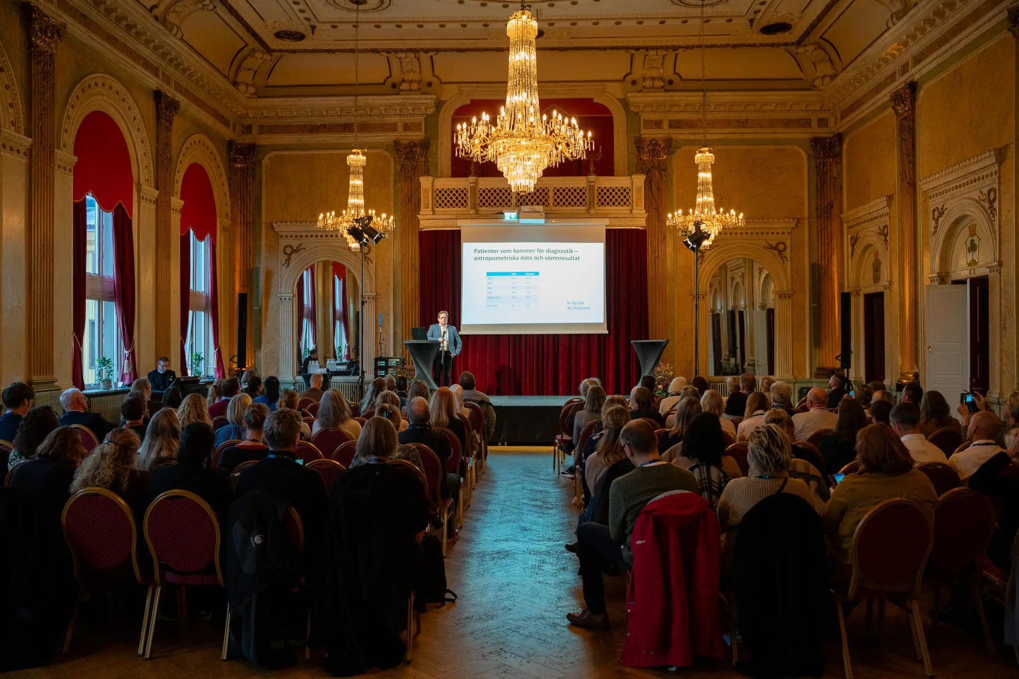 En publik lyssnar till en föreläsning på en konferens.