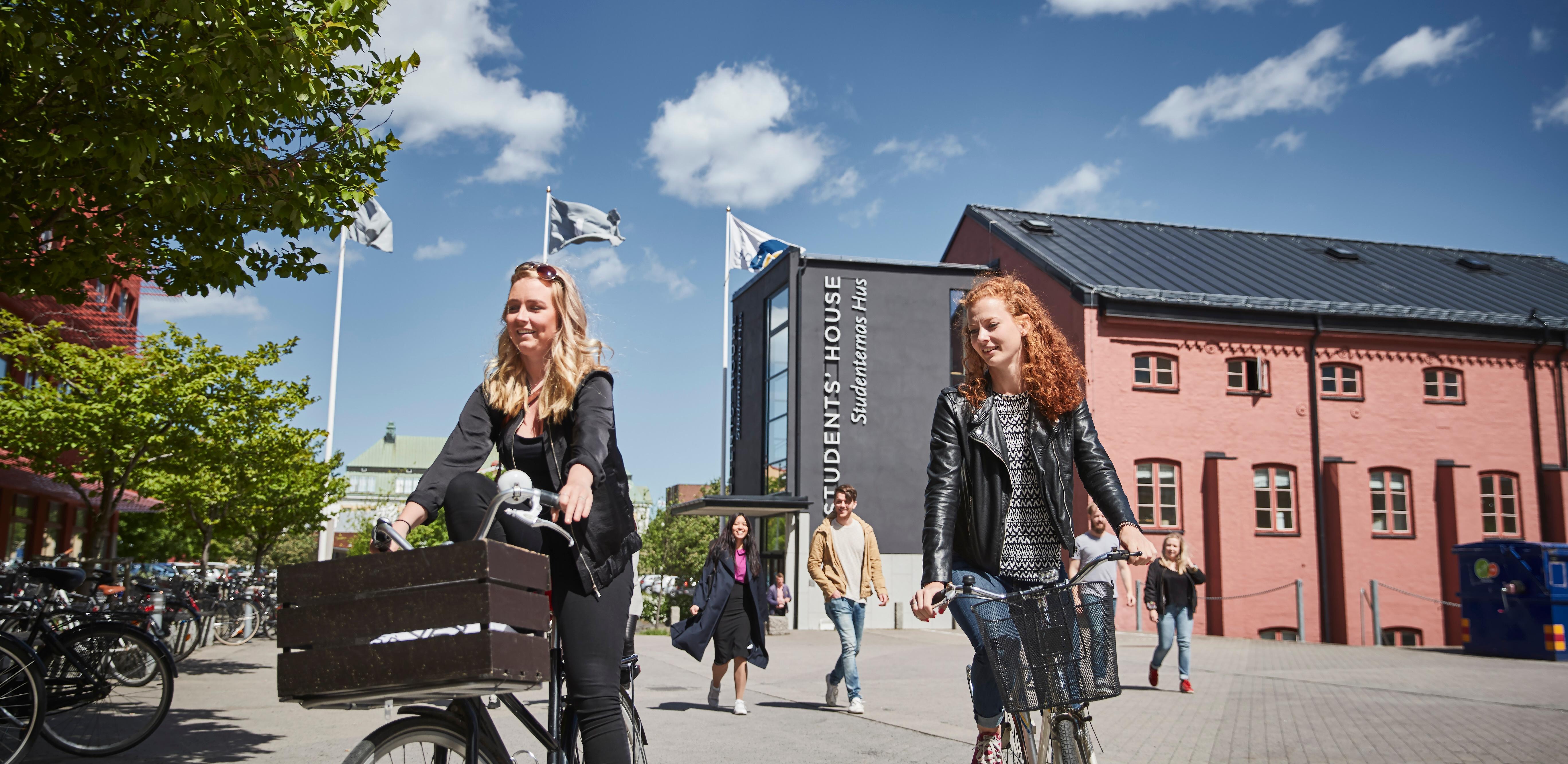 Två kvinnor är påväg att parkera sina cyklar på campus