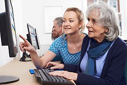 Young female tutor helps elderly woman in a computer class. 